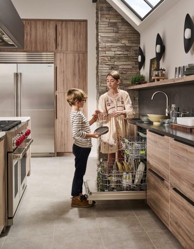Two children using Cove dishwasher in luxury kitchen.