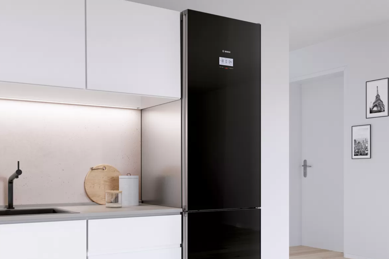 A modern kitchen features a black, two-door refrigerator with a digital display, next to white cabinets and a sink, with artwork visible in the background.