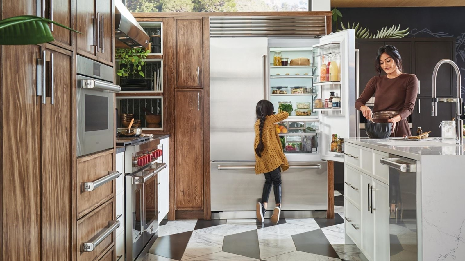 A kitchen scene shows someone using a bowl on an island and another reaching into a stainless steel fridge.