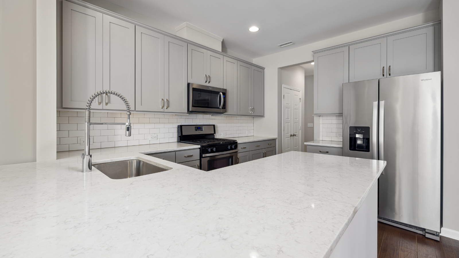 A modern kitchen interior featuring grey cabinetry, white countertops, and stainless steel appliances.