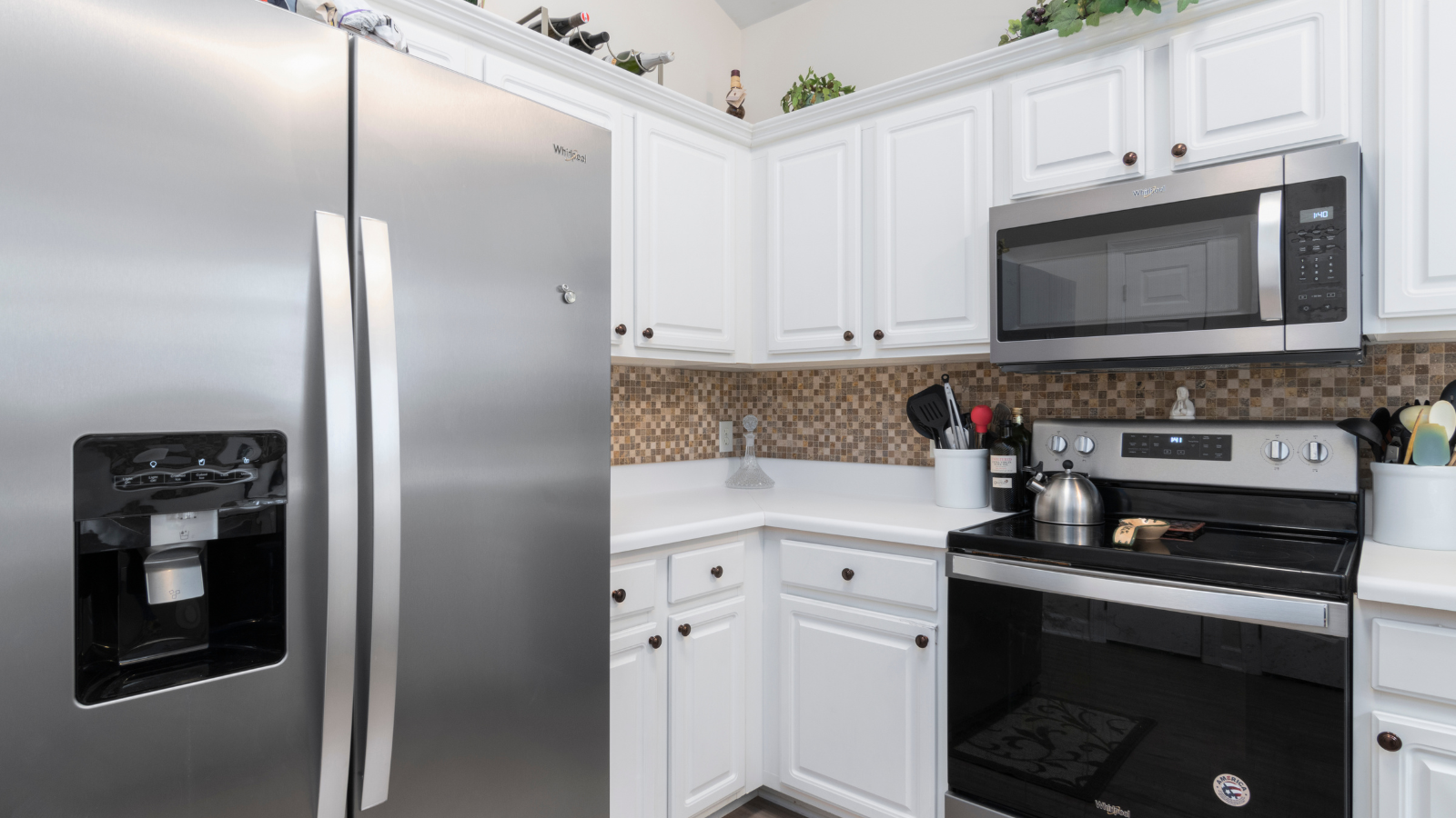 A kitchen corner displaying white cabinets, a mosaic backsplash, and a suite of stainless steel appliances.