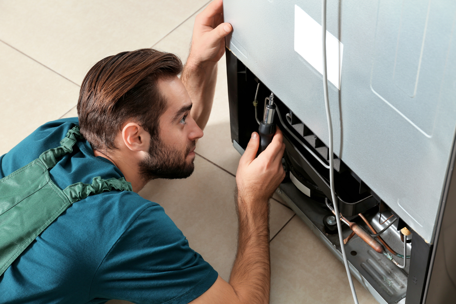 Technician checking inside a refrigerator and behind it to find why the refrigerator is leaking water.
