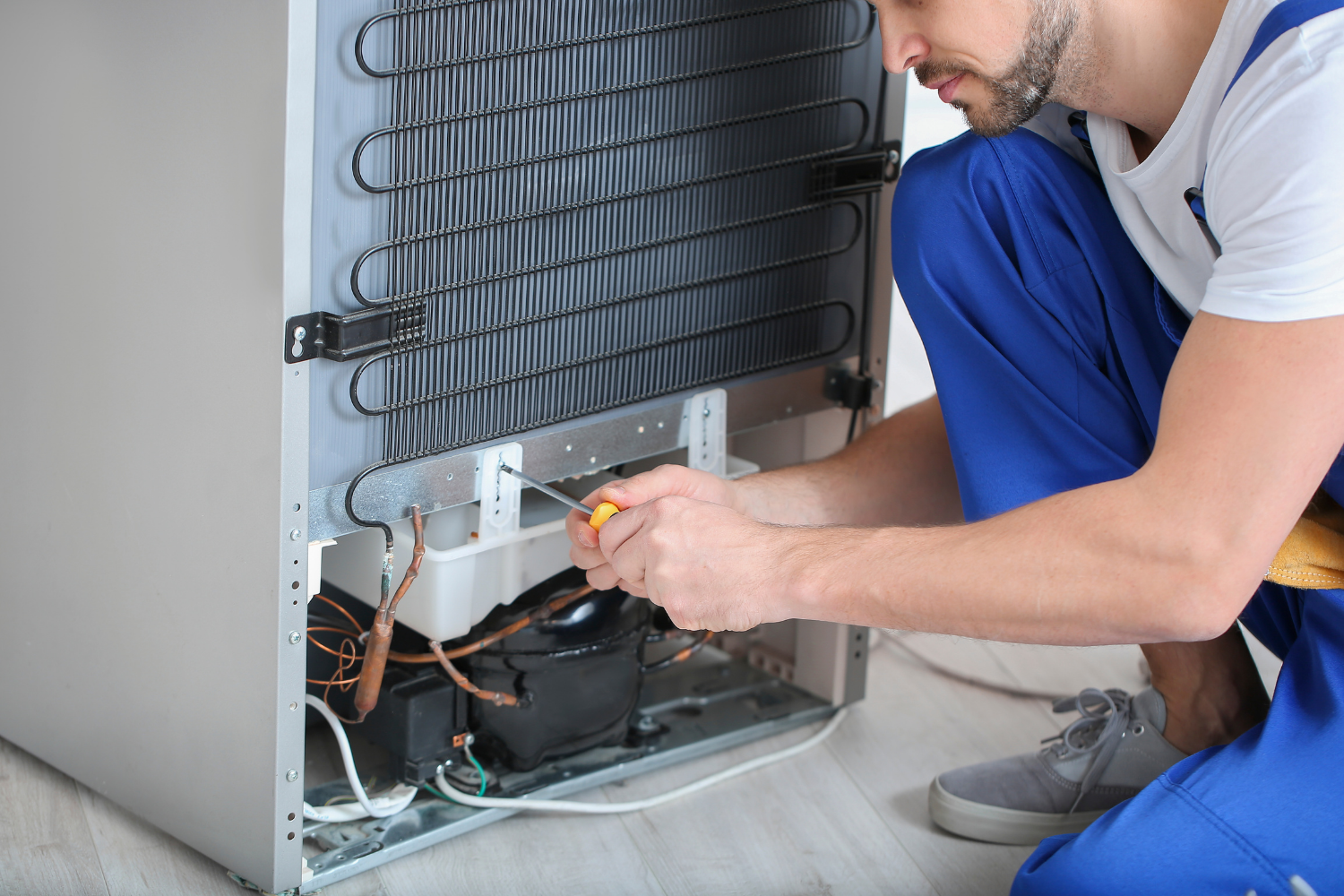 Technician cleaning refrigerator condenser coils as part of routine fridge maintenance to extend appliance life.