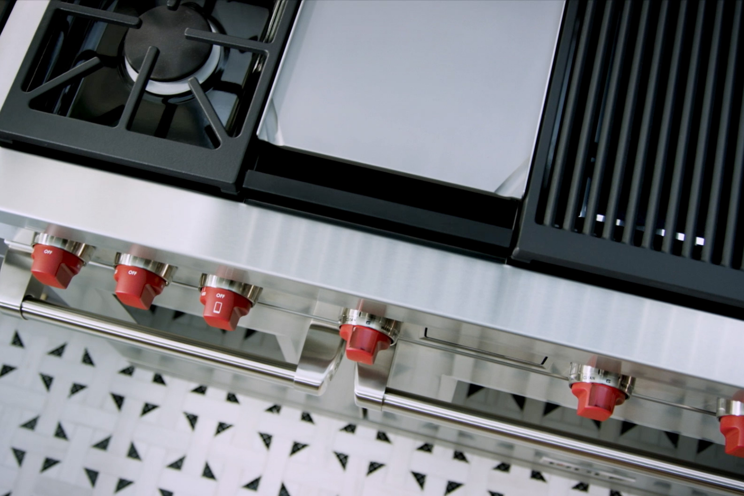 High-end kitchen range with gas burner, griddle, grill, and red control knobs.