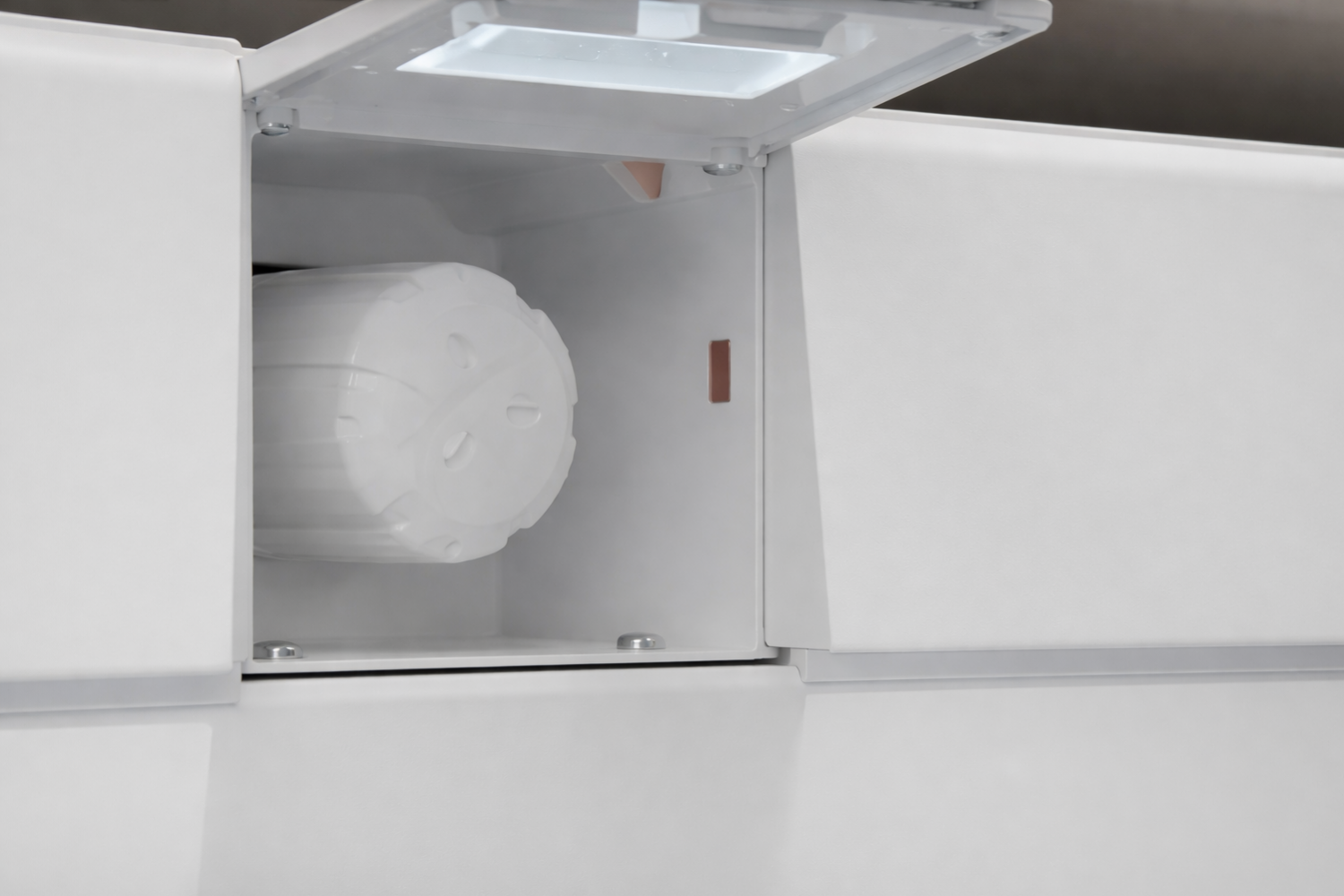 A white cylindrical water filter with a textured surface is inside an open white compartment with a light on the inside of the lid.