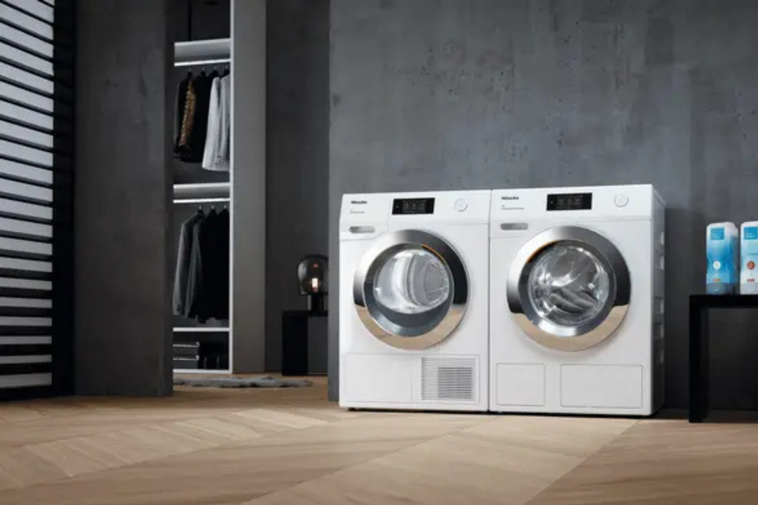 A white Miele washing machine and dryer are side-by-side in a modern room with a closet and a wooden floor.