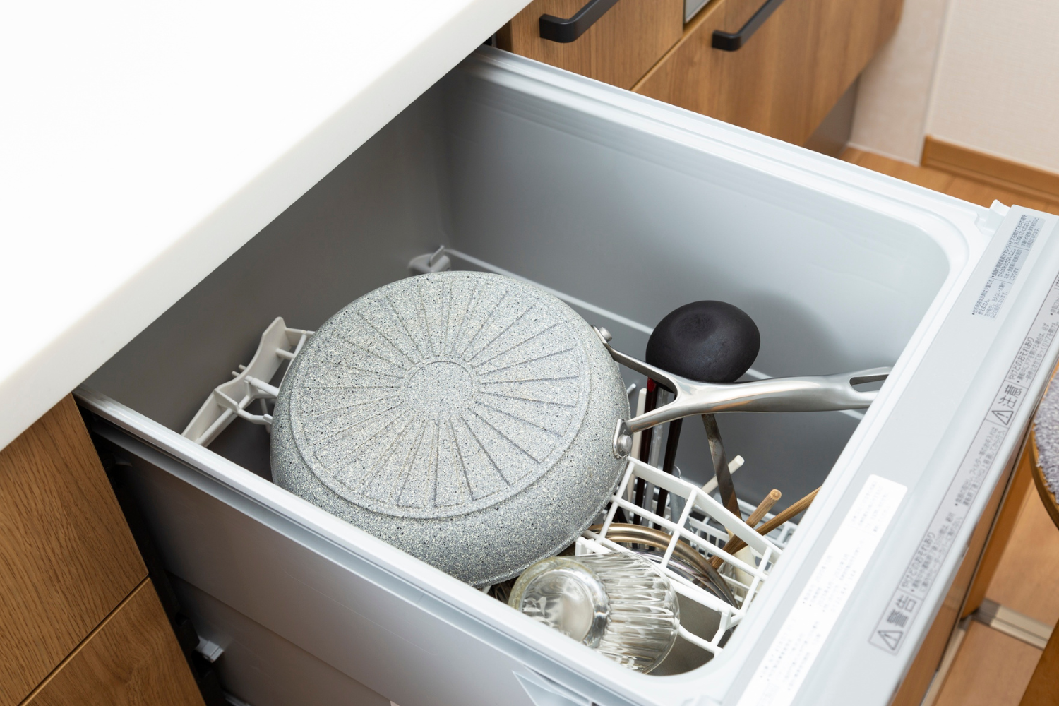 A dishwasher rack holds a grey frying pan, a black pot lid, and various utensils.