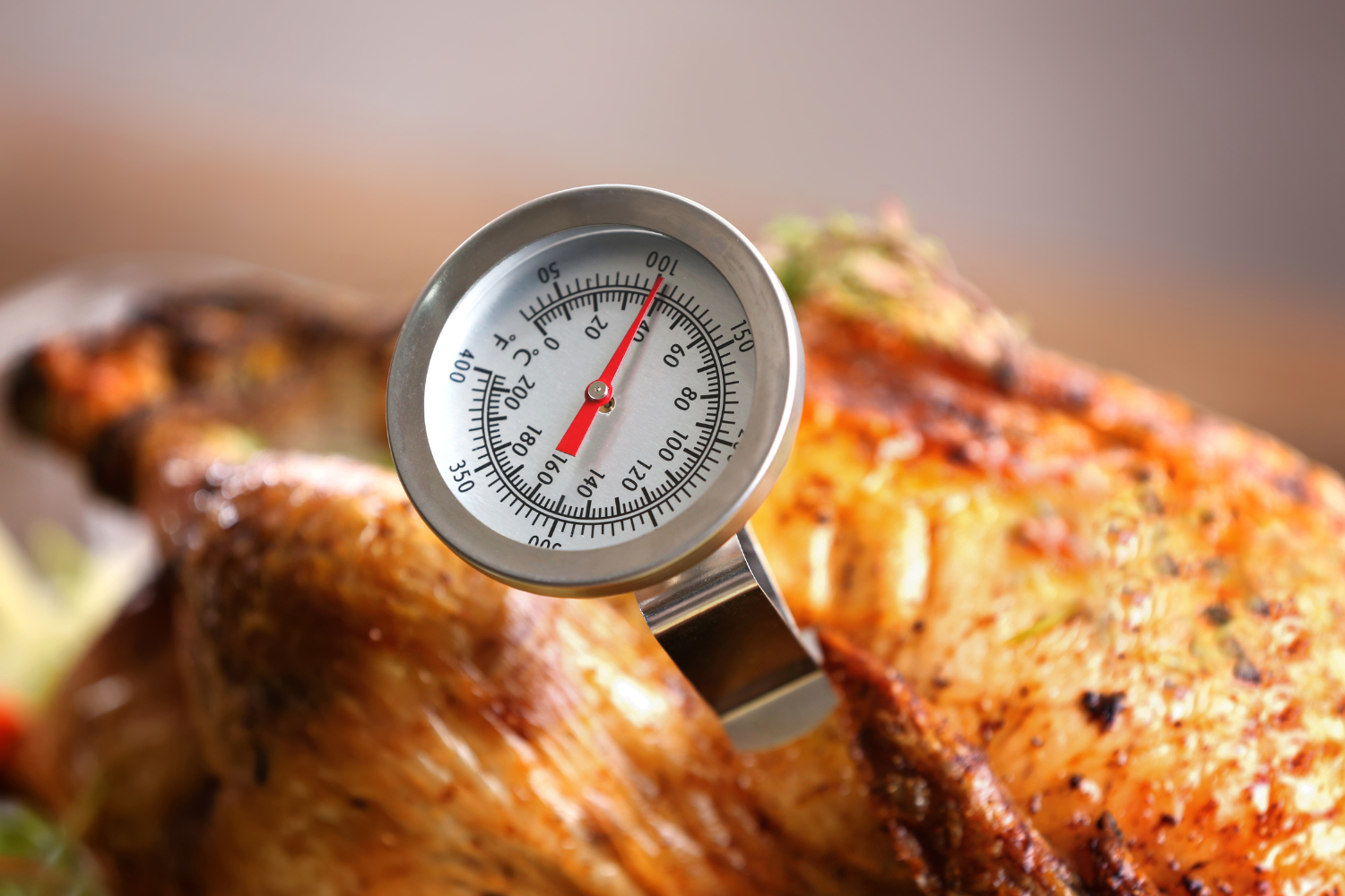 A meat thermometer is inserted into a golden-brown roasted chicken.