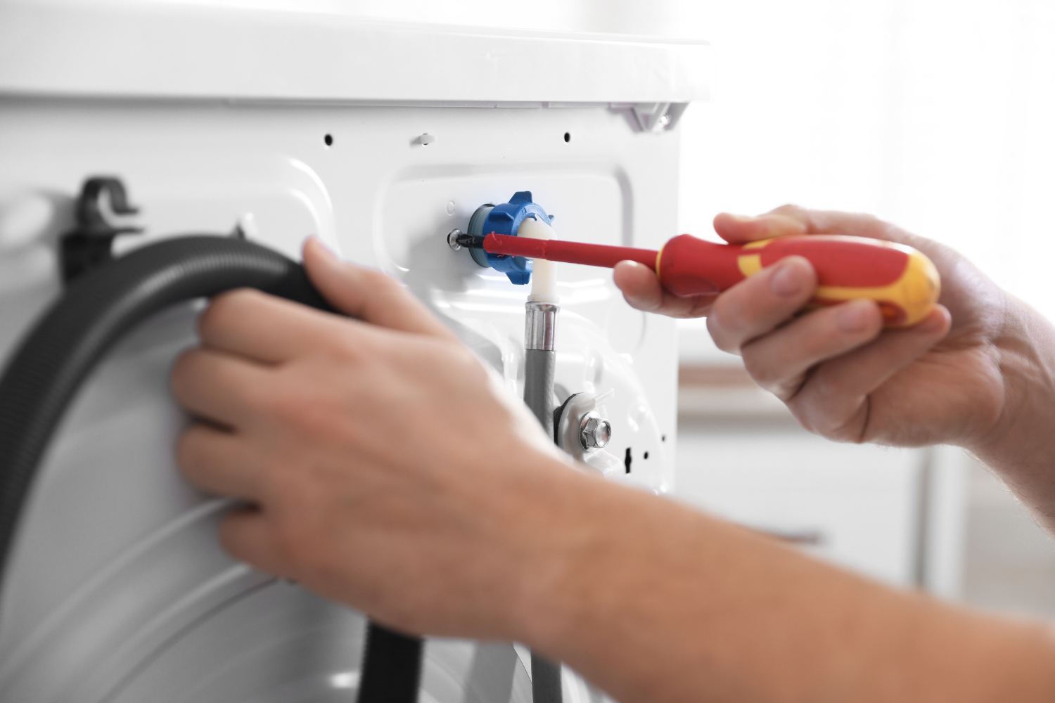 A person is using a screwdriver to tighten a blue fitting on the back of a white appliance.