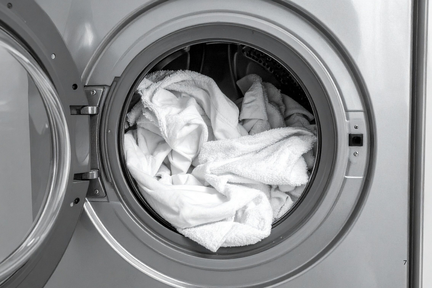 A front-loading washing machine with its door open, revealing a load of white laundry inside.