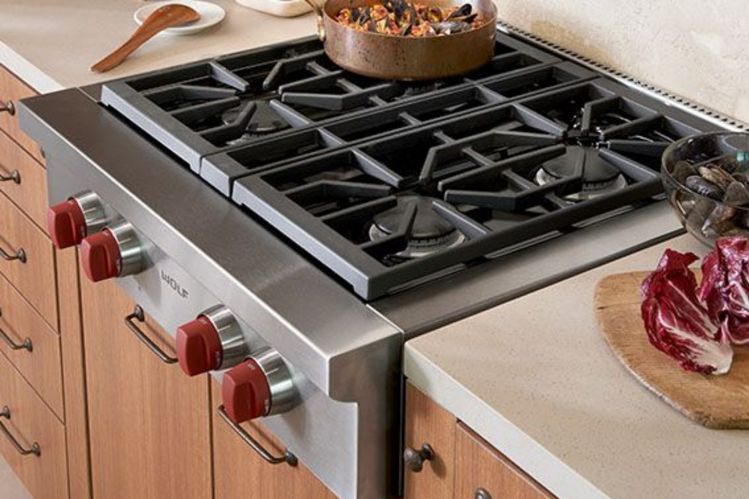 A professional Wolf gas range with red control knobs and a pot of food cooking on the grates, next to radicchio on a cutting board.