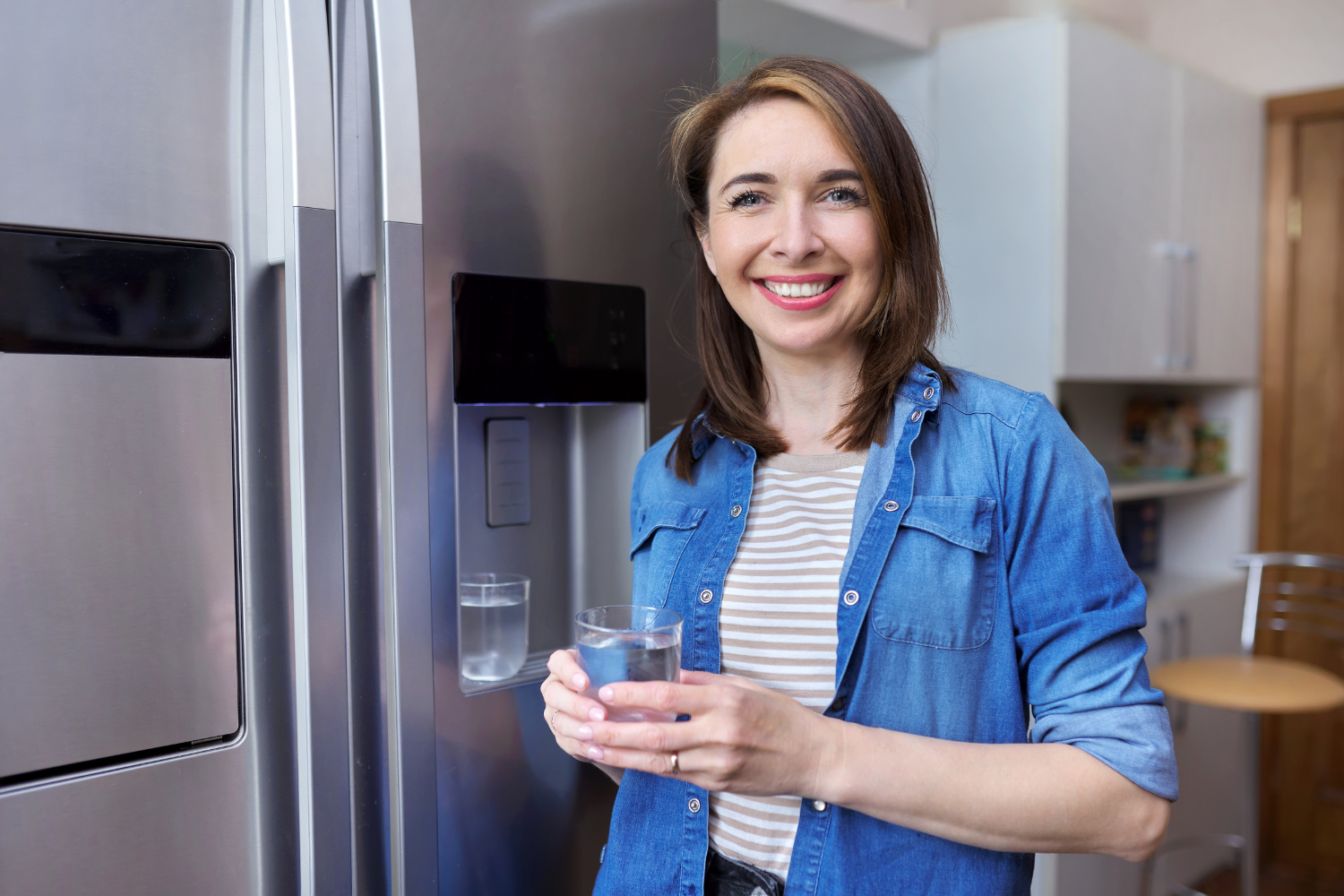 Woman holding a glass of water from a refrigerator after water filter replacement