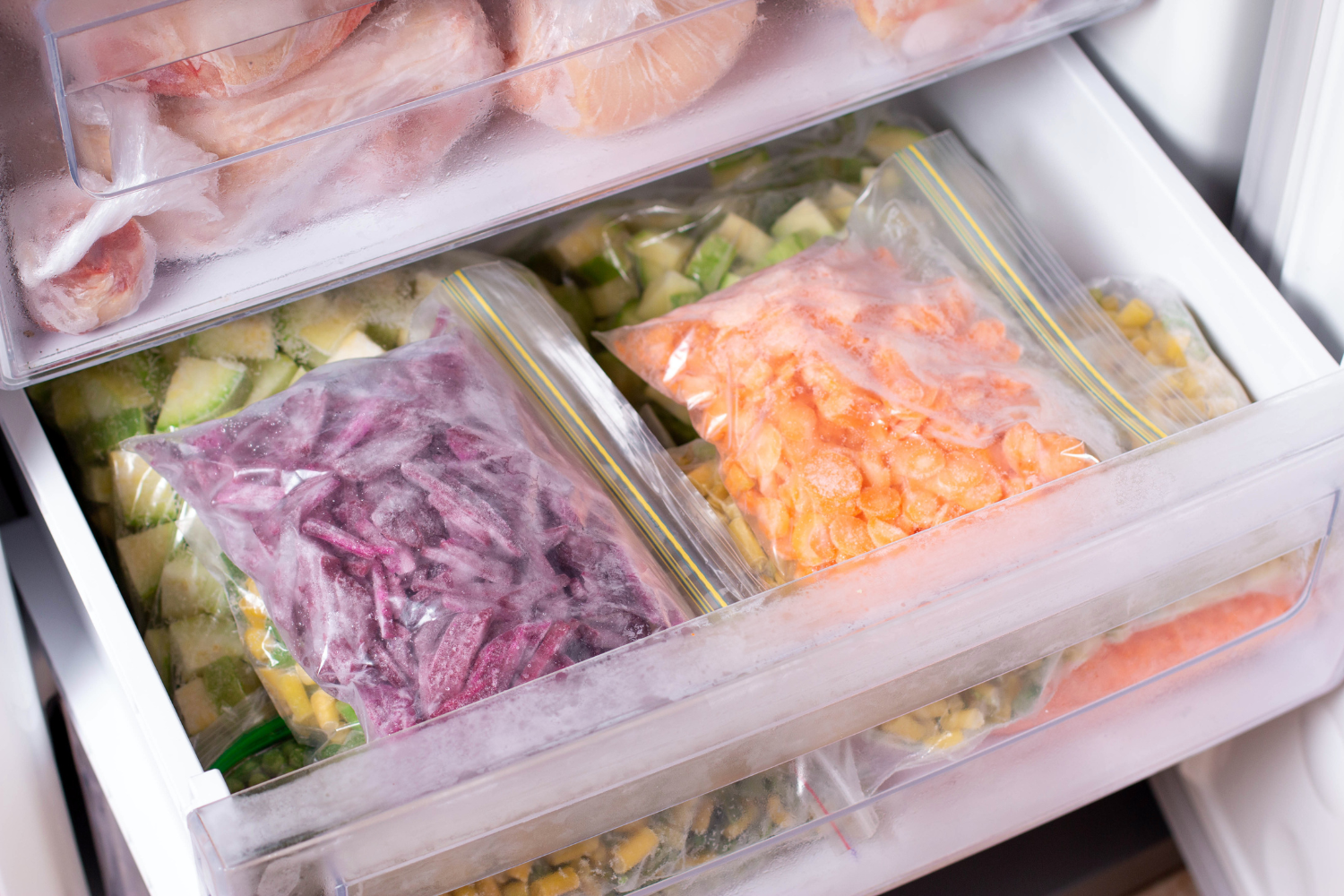 Freezer drawer organized with bags of frozen vegetables and meat, illustrating how food storage can be affected when the freezer door seal is not sticking tightly.