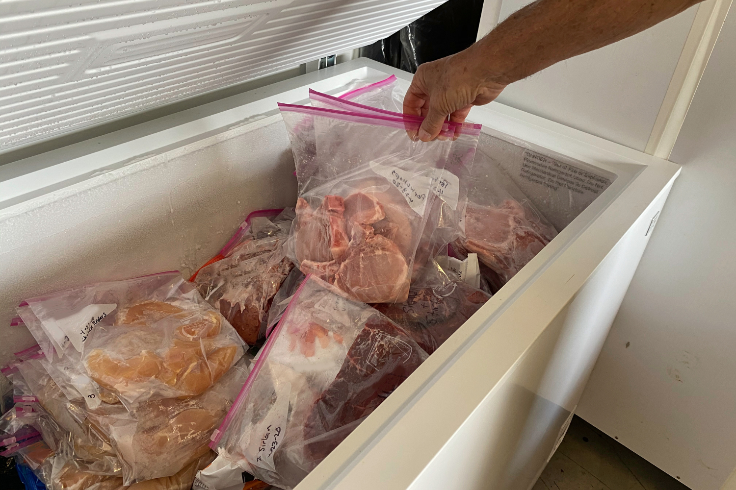 Open chest freezer filled with labeled bags of frozen meat, showing how frost buildup along the edges may indicate the freezer door seal is not closing properly.