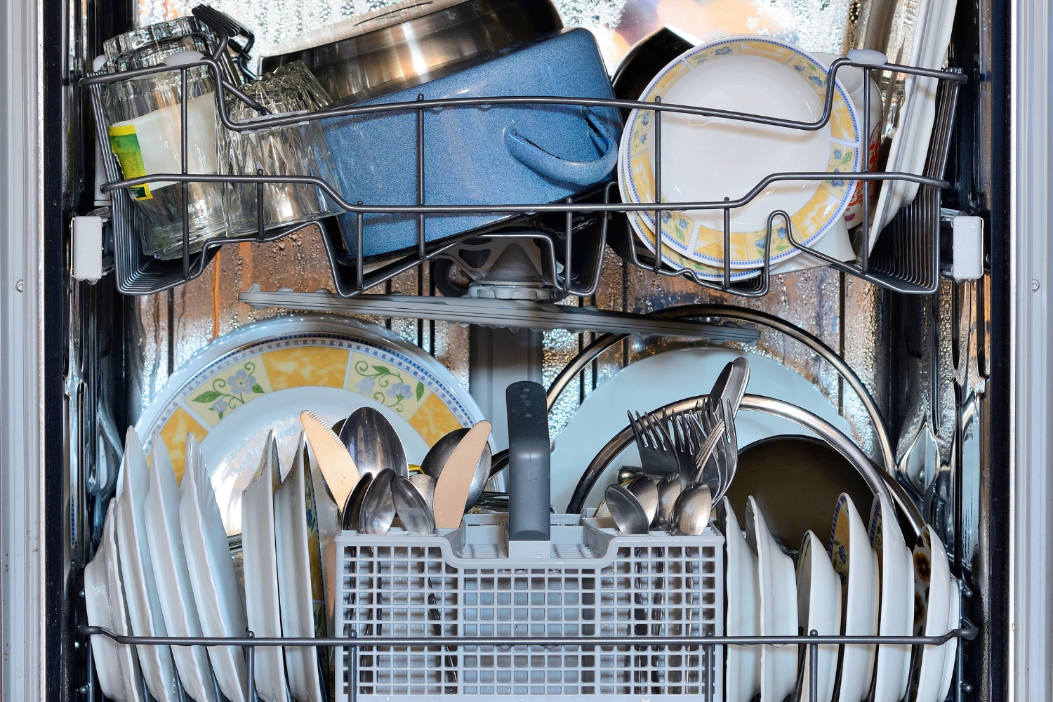 Overloaded dishwasher filled with plates, cups, and utensils showing a common cause of dishwasher white residue and poor rinsing.