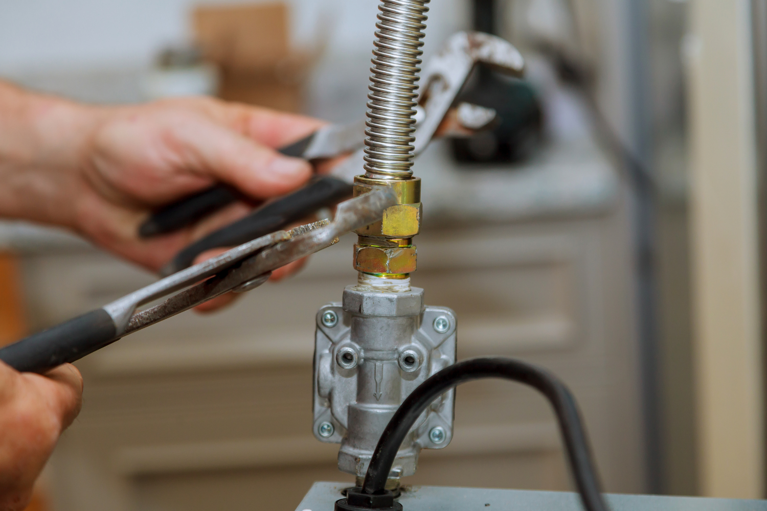 Close-up of a technician using tools to repair a flexible gas line connection on a kitchen appliance.