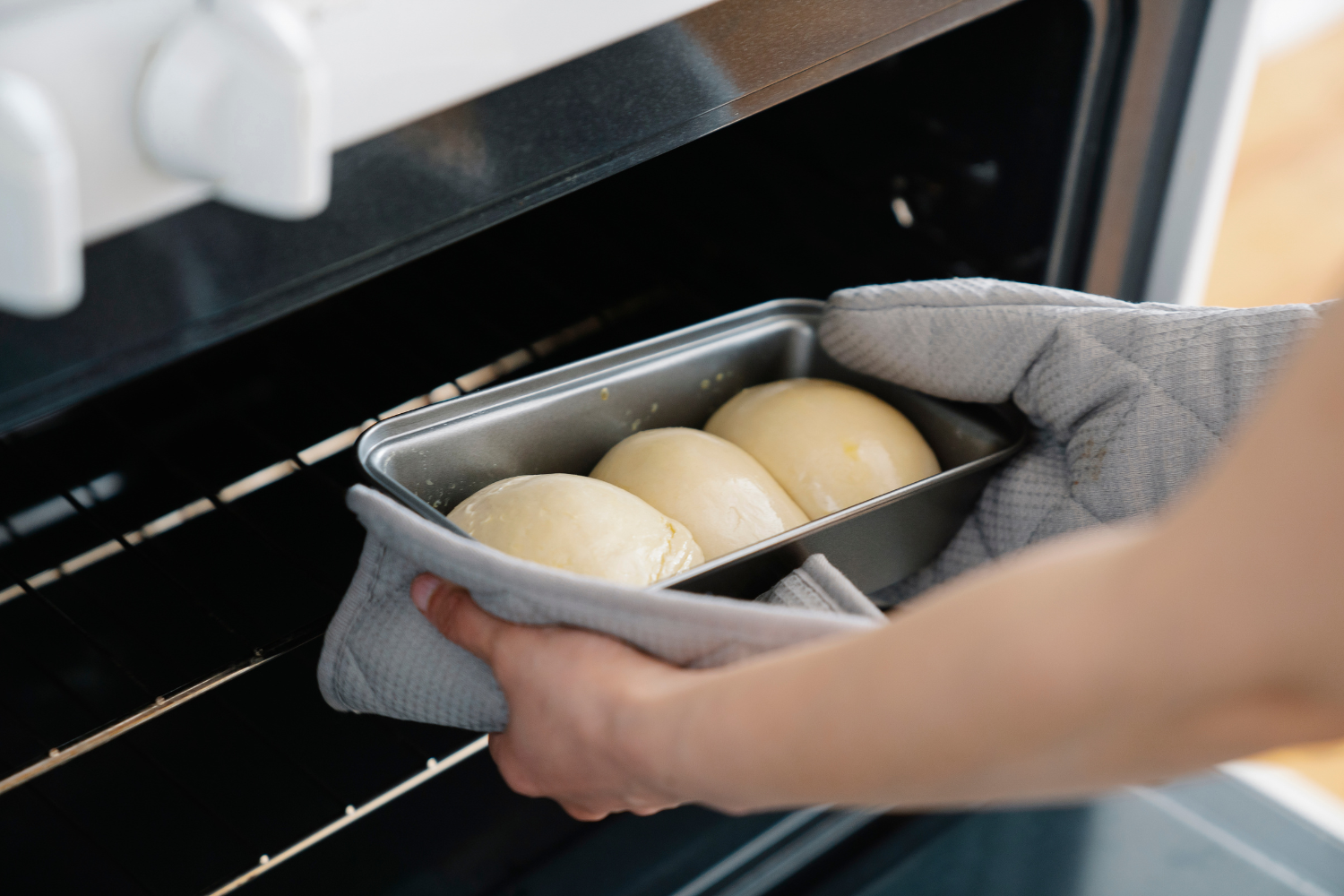 Hands placing a loaf pan with dough into an oven during home baking.
