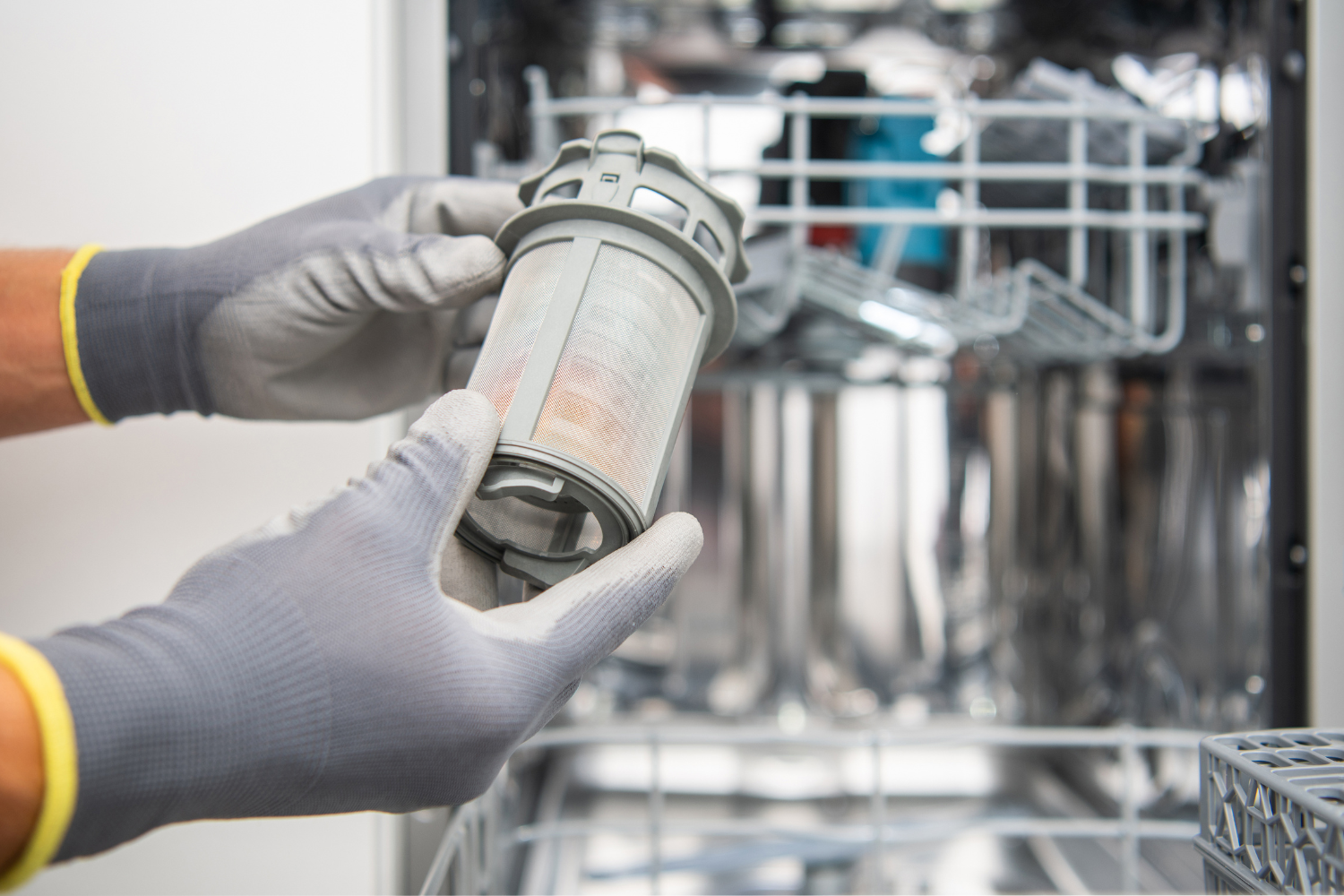 Hands wearing gray gloves holding a dirty dishwasher filter.