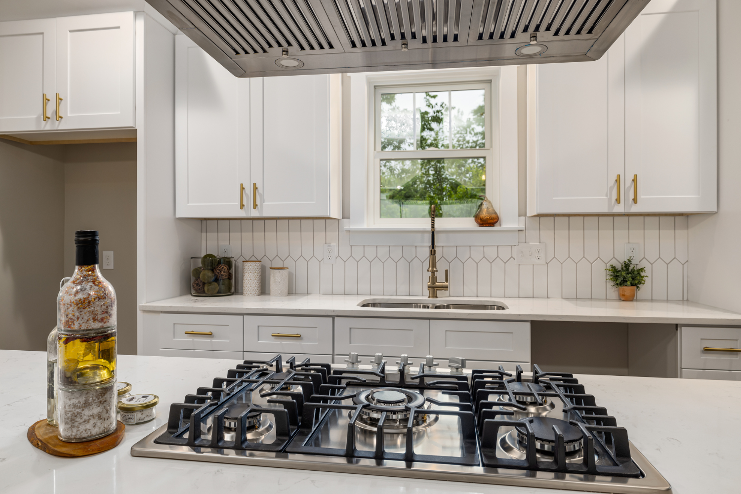 A modern kitchen with white cabinets, gold hardware, a stainless steel range, and a window above the sink.