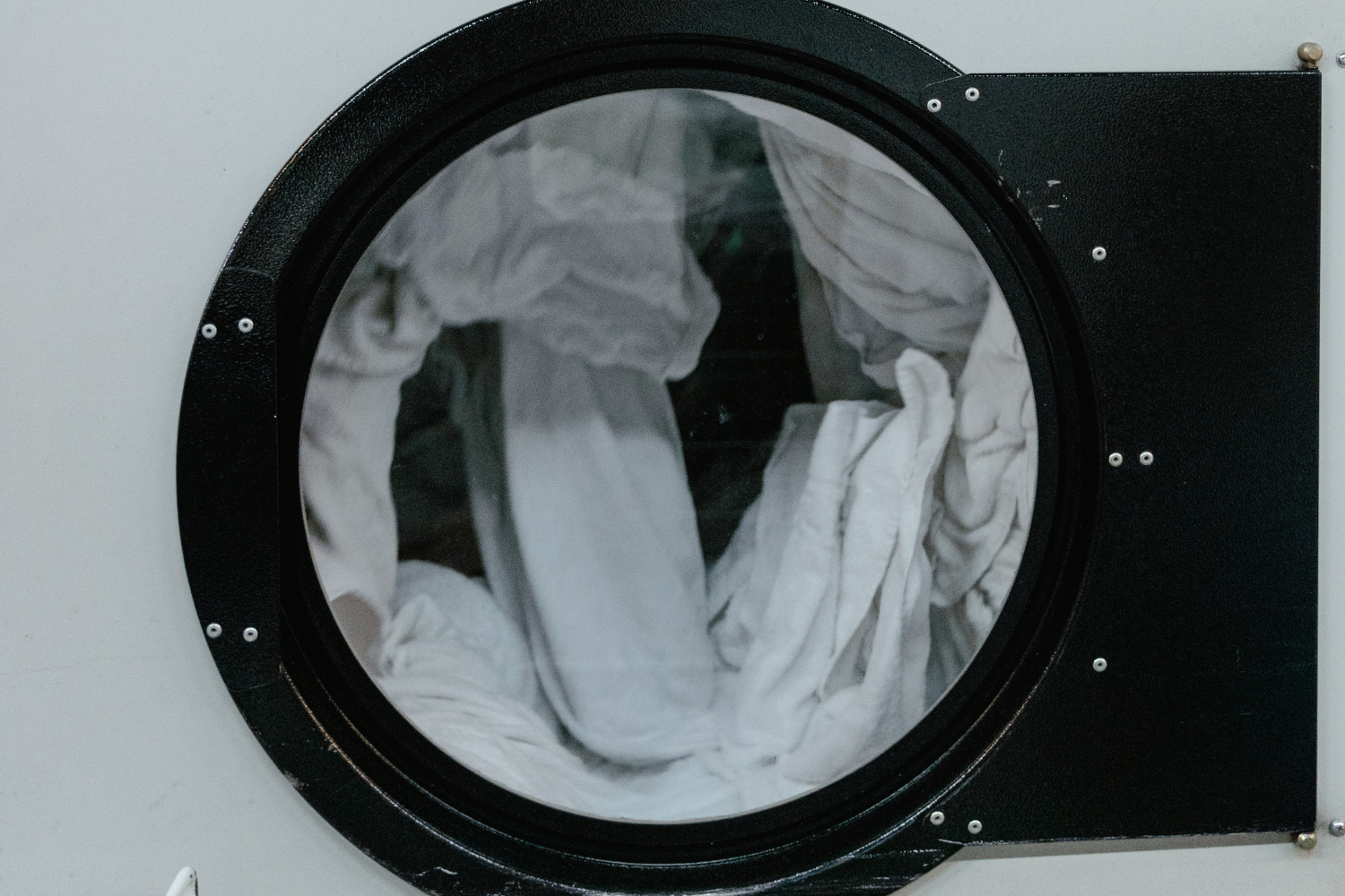A close-up view through the glass door of a dryer, showing white laundry tumbling inside.
