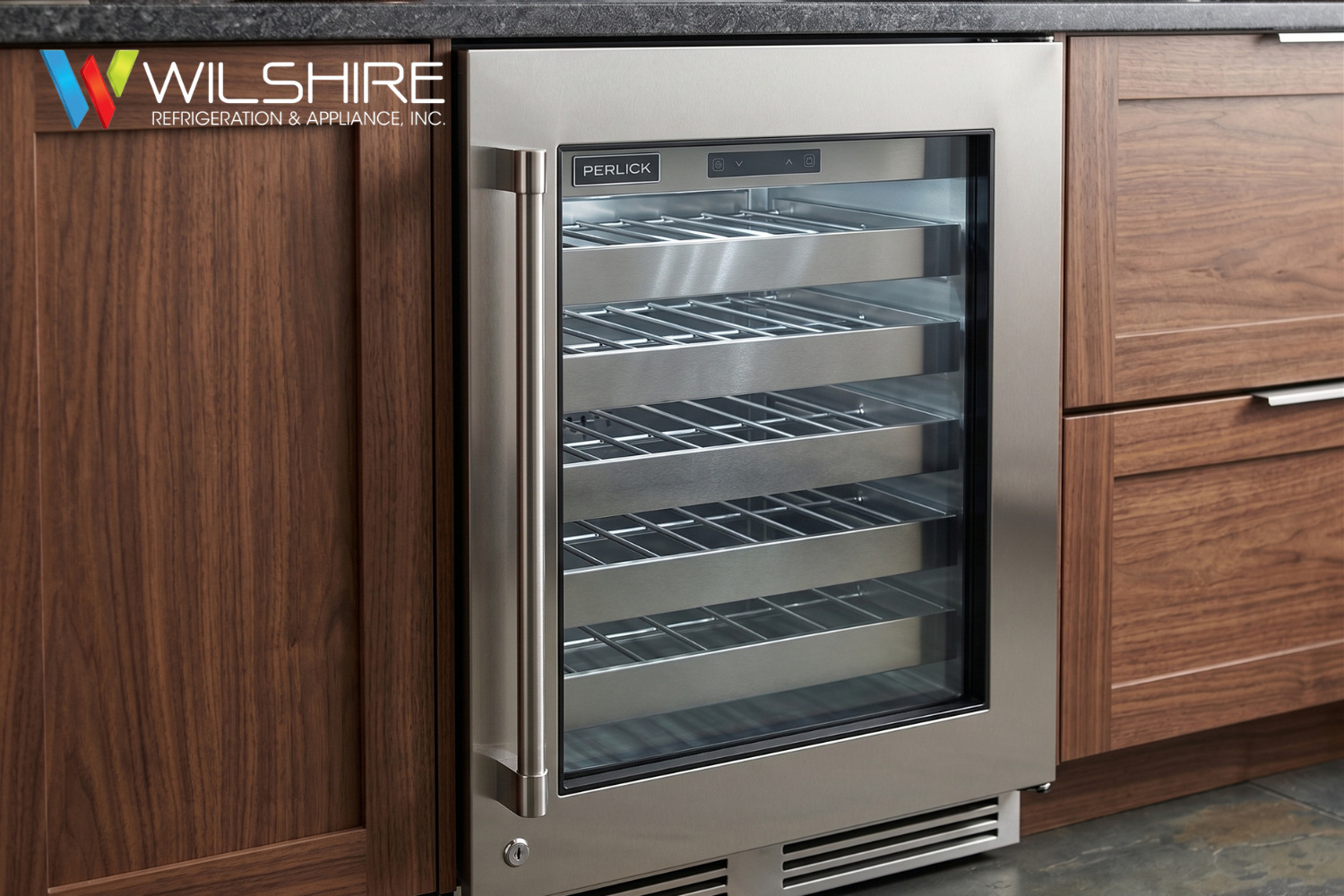 Built-in stainless steel glass-front Perlick refrigerator drawer with multiple shelves, set into a wooden cabinet, showing neatly arranged items inside.