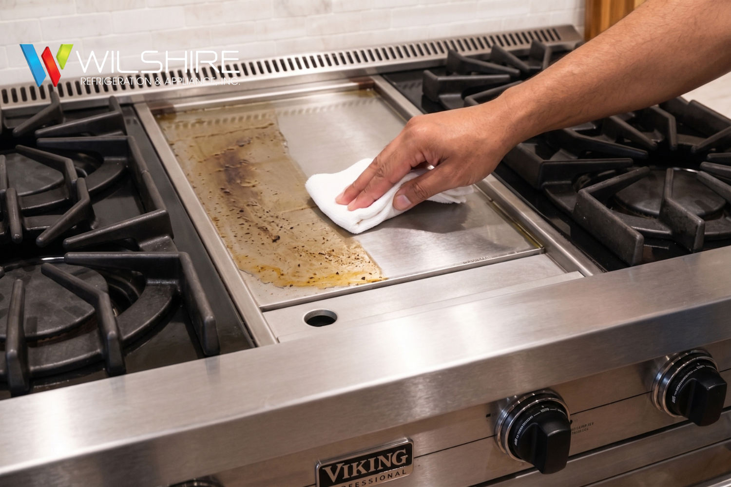 Hand wiping grease from the griddle of a Viking Professional stainless steel range during cleaning.