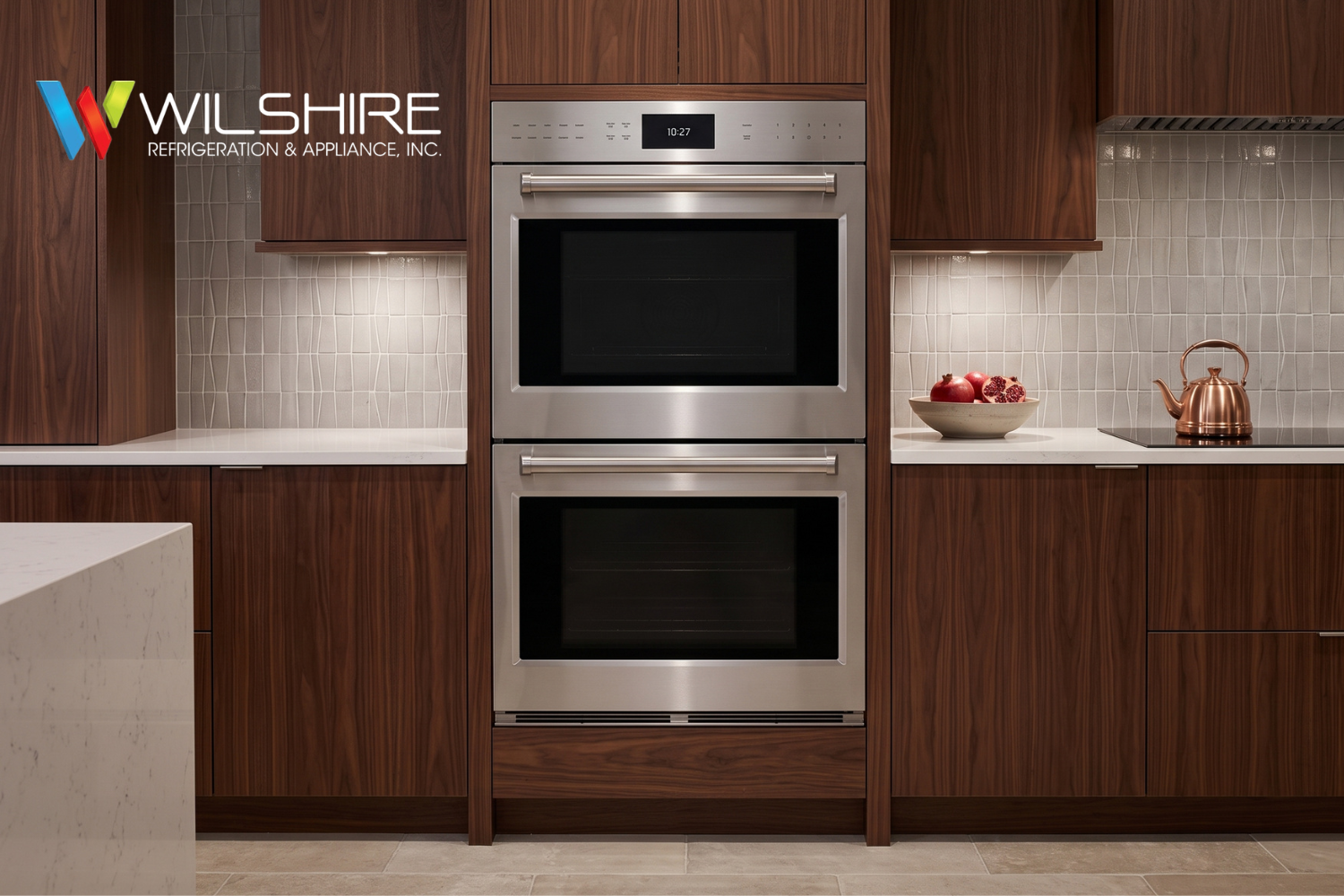 Wolf stainless steel double wall oven with digital display and red knobs, built into dark wood cabinetry with wavy tile backsplash and quartz countertop.