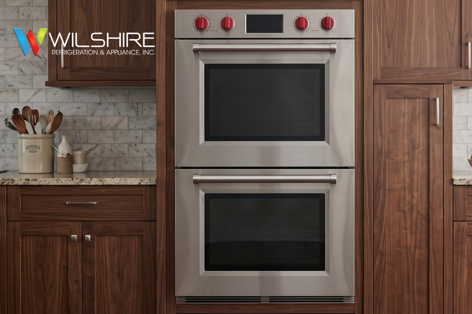 Wolf stainless steel double wall oven with red knobs, built into rich brown cabinetry with marble tile backsplash and light stone countertop.