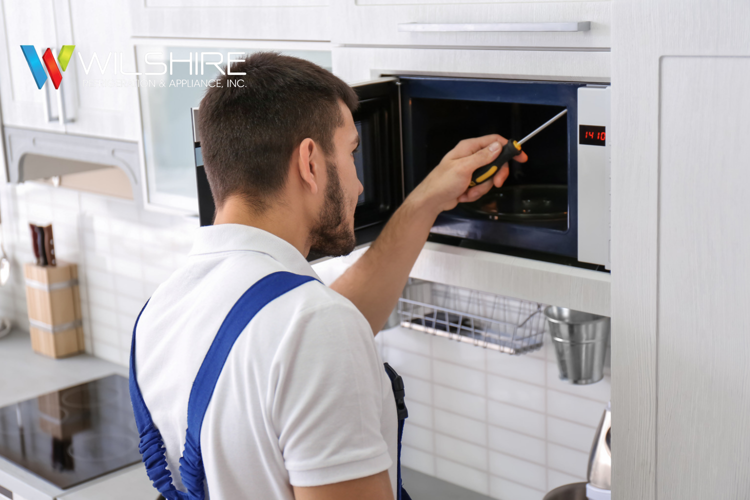 Technician inspecting and repairing a Wolf microwave turntable mechanism inside a built-in kitchen microwave.