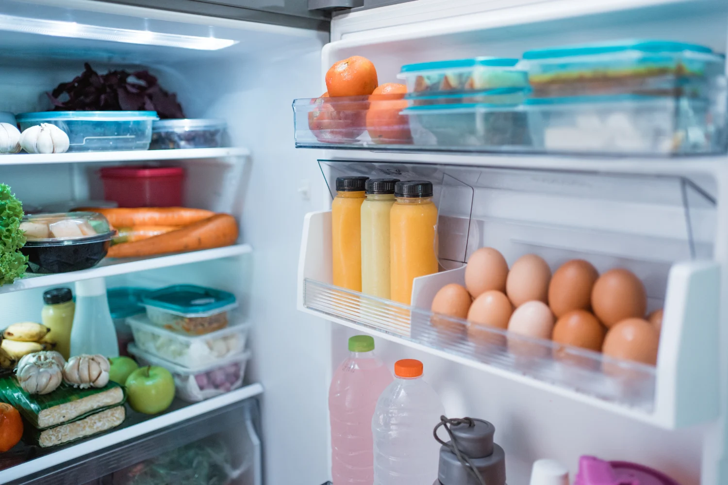 Open refrigerator with food containers, eggs, vegetables, and drinks inside, representing common Sub-Zero refrigerator repair issues related to lighting and cooling performance.
