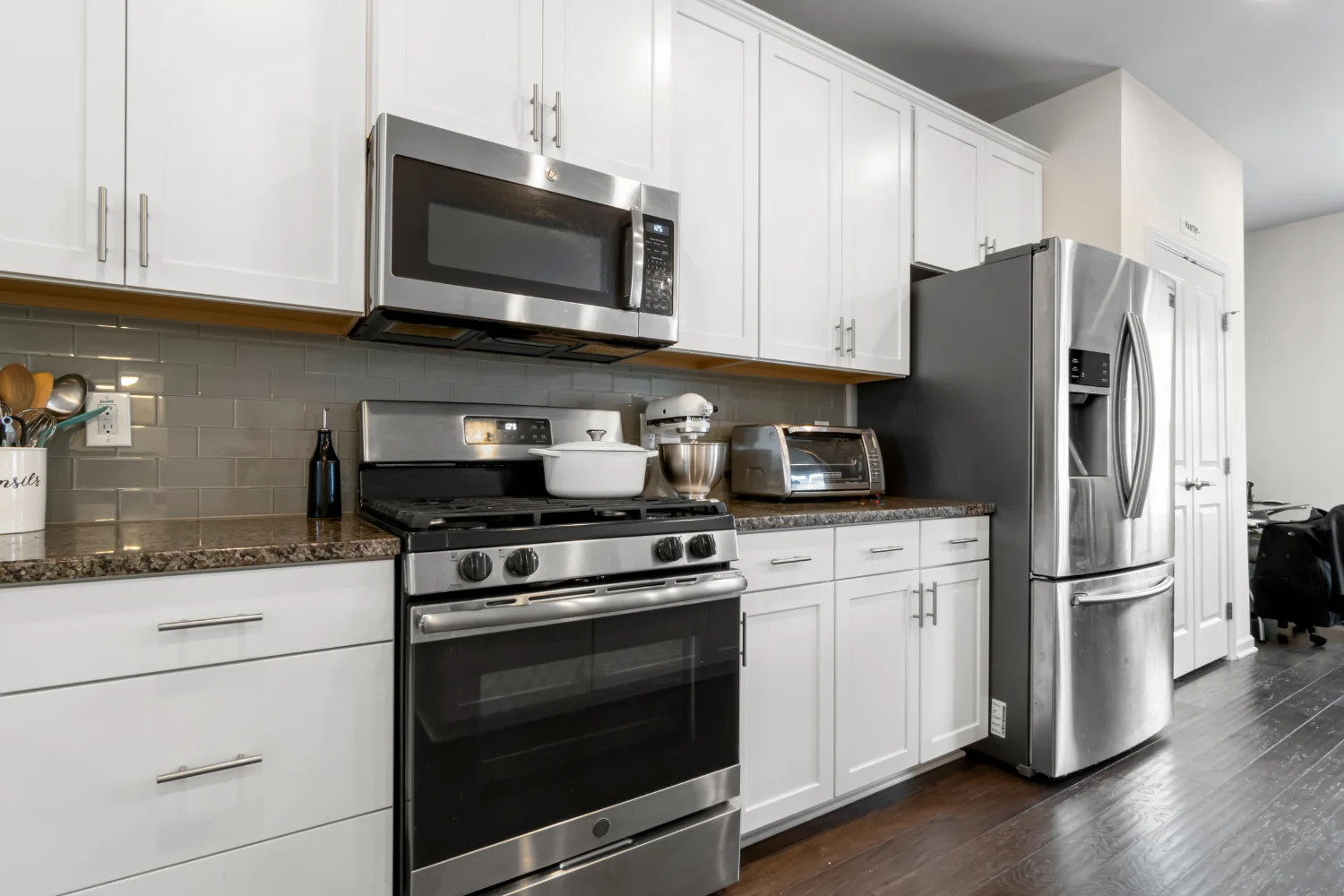 A modern kitchen with stainless steel appliances including a microwave, oven, refrigerator, and toaster. White cabinets and a granite countertop complete the look.